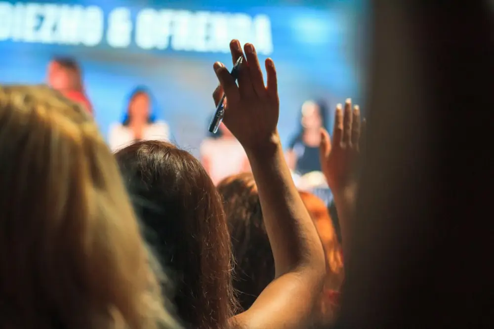 People in an audience raising their hands to ask questions at a conference, illustrating voice and audience